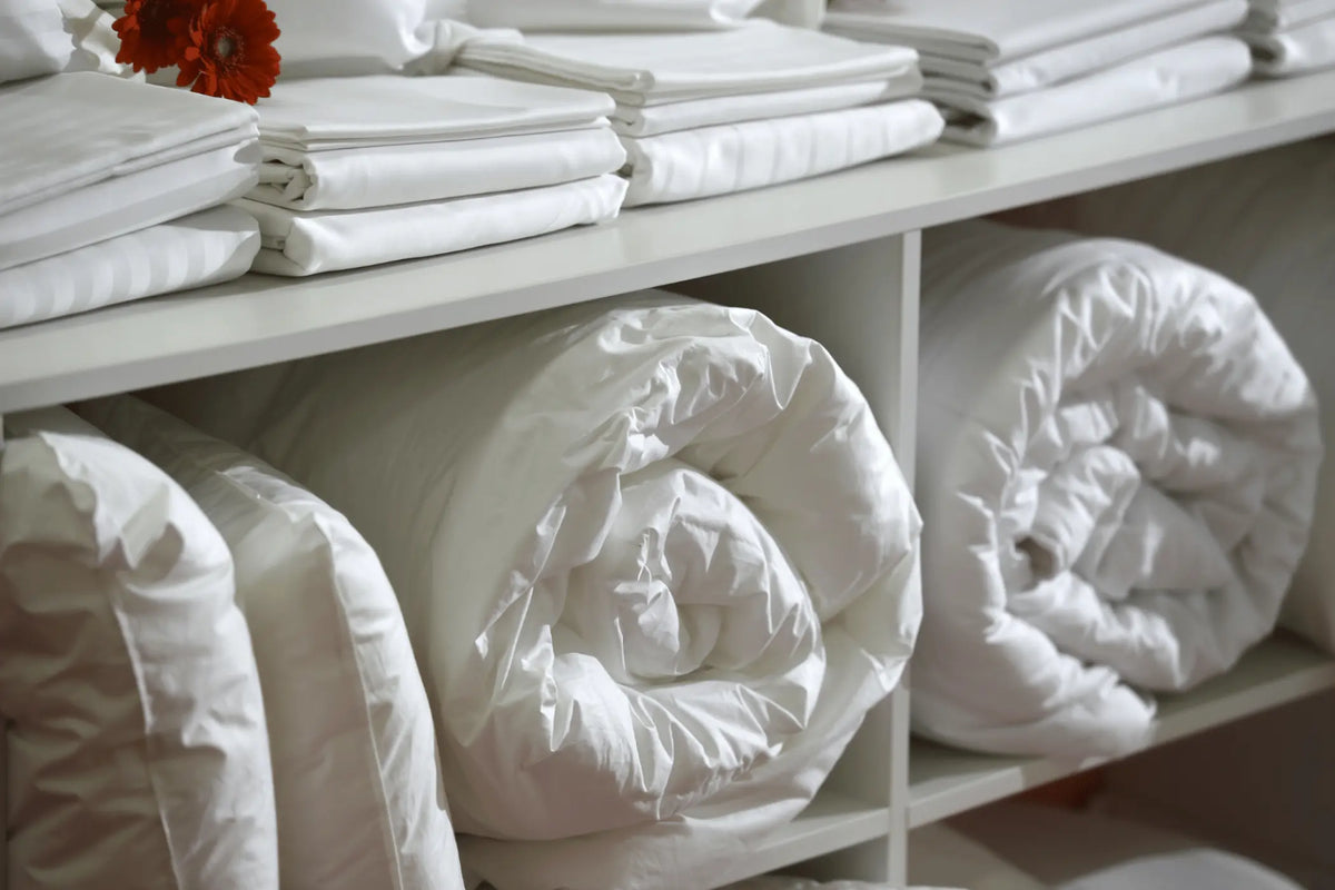 Linge de lit blanc plié et couettes rangées sur des étagères Image